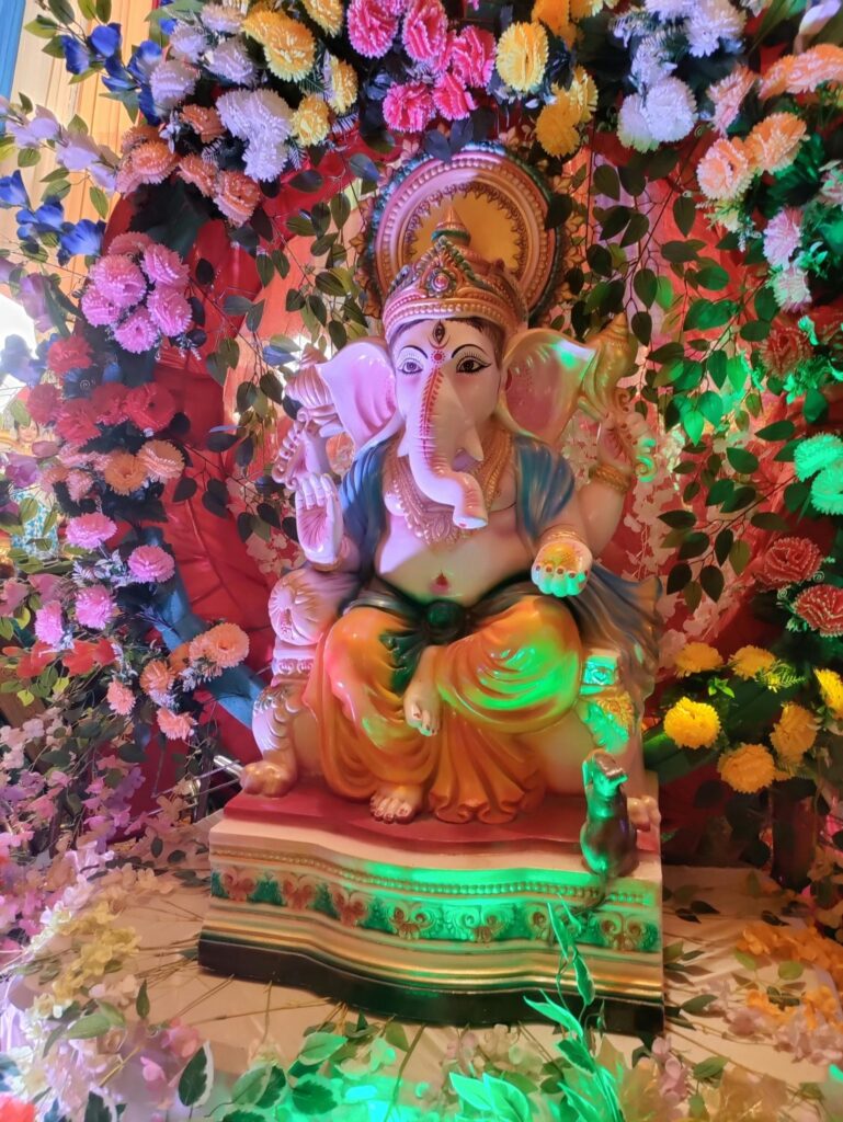 A statue of Lord Ganesha surrounded by an arrangement of multicolored artificial flowers.